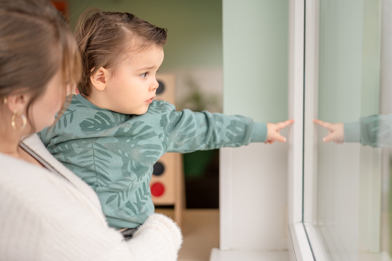 Kind wordt gedragen en wijst naar buiten door het raam